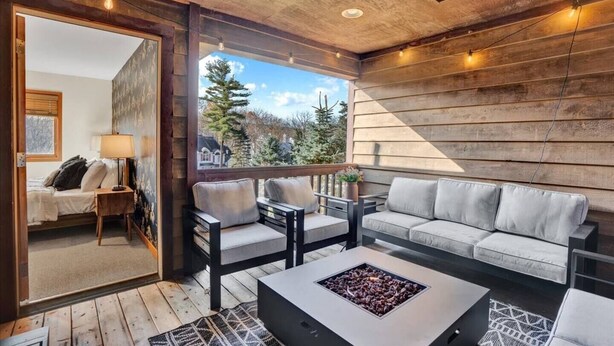 Un espace extérieur accueillant avec des sièges confortables, un foyer, des murs en bois et une vue sur les arbres.