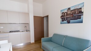 A modern kitchen with white cabinets, a sink, and a stove. There is a blue sofa and a painting of a castle on the wall. - DimmiDiRimini (Rimini)