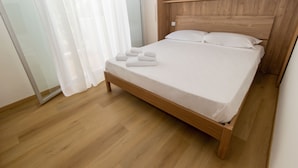 A neatly made bed with white linens and folded towels, a wooden headboard, and a wooden floor. - DimmiDiRimini (Rimini)