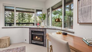 Una sala de estar moderna con chimenea, ventanas amplias y vistas a árboles.