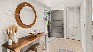 A modern interior with a wooden console table, a round mirror, and a white brick wall.