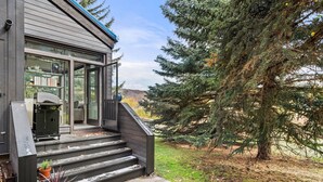 A modern house with a large glass door, steps leading to a porch, and a large evergreen tree in the yard.