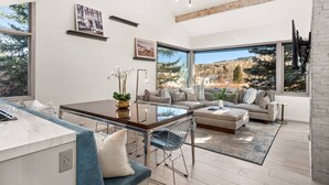 A modern living room with a large window, a sofa, a coffee table, and a dining area.