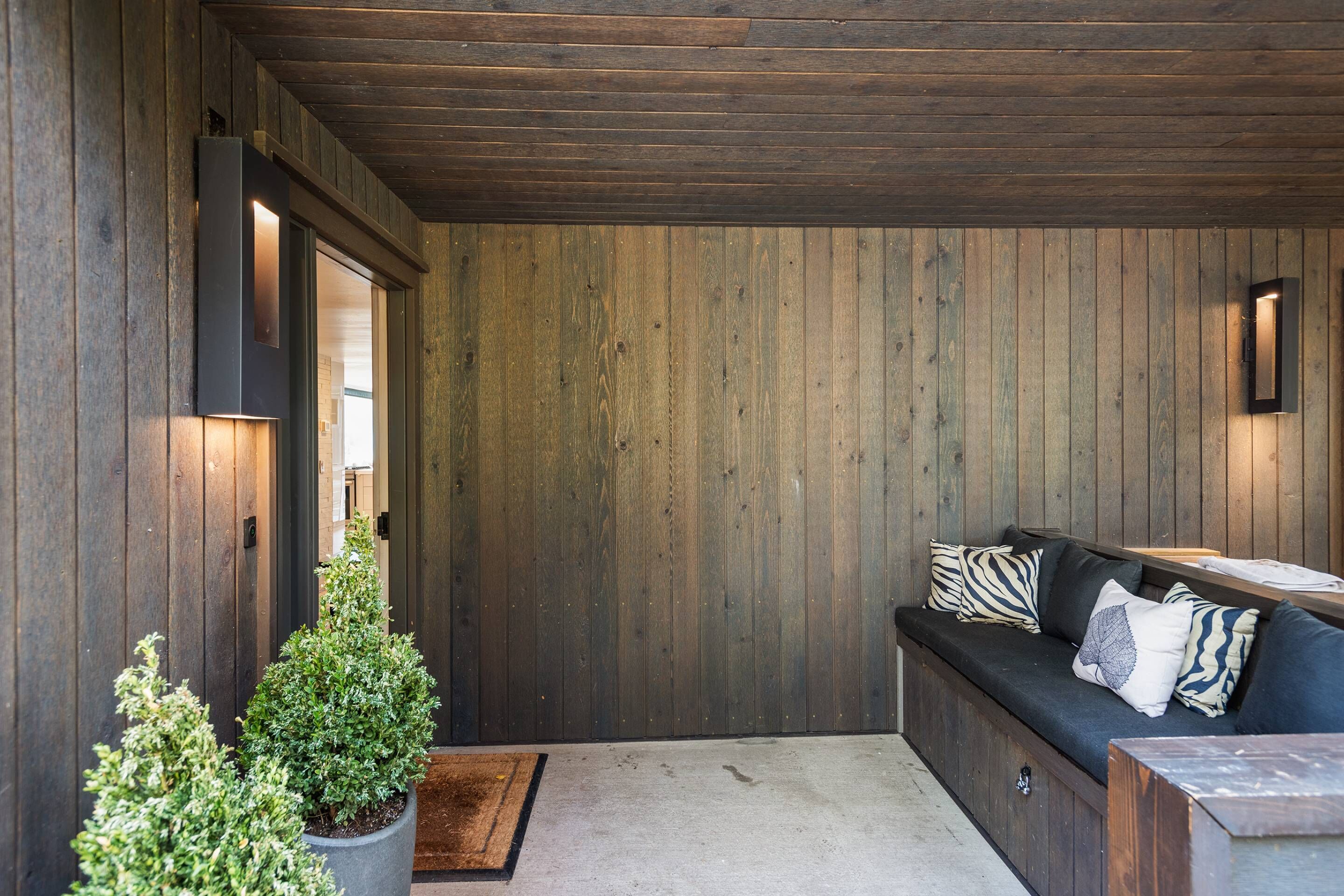 Un interior moderno con una pared de madera, un sofá negro con cojines estampados y una pequeña planta en maceta.
