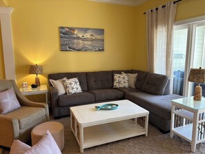 A living room with a sofa, armchair, coffee table, and a painting on the wall. - Family Tides, Litchfield condo (Pawleys Island)