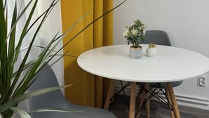 Una habitación con una mesa redonda blanca, dos sillas grises, una planta en maceta y un pequeño florero con flores.
