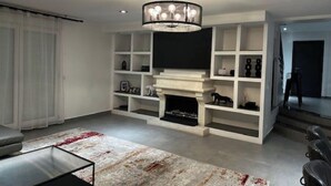 Een moderne woonkamer met een open haard, inbouwplanken en een kroonluchter.