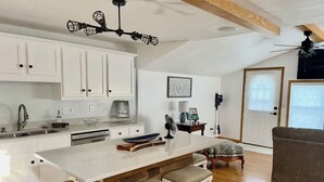 A modern kitchen with white cabinetry, a large island with bar stools, and a ceiling fan. - T’is Our Cottage:Modern Lakefront fall colors & football relax Just off toll Rd  (Howe)