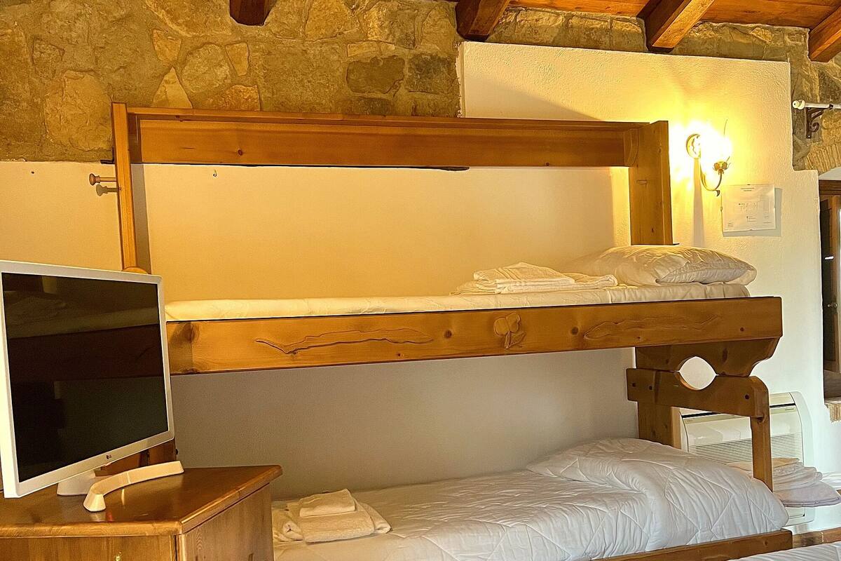Una cama litera con cabecera de madera, una mesita de noche con televisor de pantalla plana y una pared de piedra.