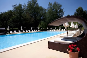 Piscina con sillas de descanso y sombrillas, rodeada de árboles.