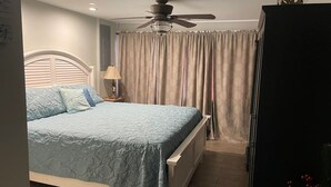 A bedroom with a bed, a ceiling fan, a nightstand with a lamp, and a wardrobe. - 01) Hidden Treasures of Treasure Island NPR (New Port Richey)