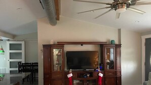 A living room with a wooden entertainment center, a ceiling fan, and a flat-screen TV. - 01) Hidden Treasures of Treasure Island NPR (New Port Richey)