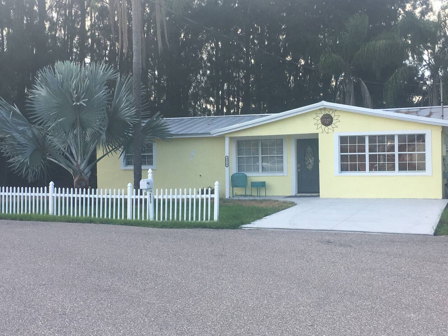 A yellow single-story building with a white picket fence, a mailbox, and a small porch area.