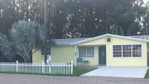 A yellow single-story building with a white picket fence, a mailbox, and a small porch area. - 01) Hidden Treasures of Treasure Island NPR (New Port Richey)