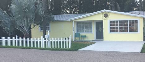 A yellow single-story building with a white picket fence, a mailbox, and a small porch area.