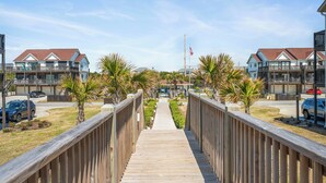 Un muelle de madera que conduce a una zona residencial con casas, una bandera y automóviles estacionados.