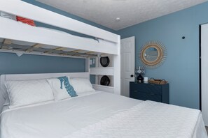 A bedroom with a bunk bed, a dresser, a mirror, and a door.