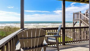 Terraza de madera con dos sillas Adirondack con vistas a la playa.