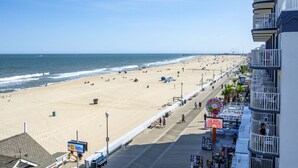 A beach with a boardwalk, shops, and a Ferris wheel in the distance.