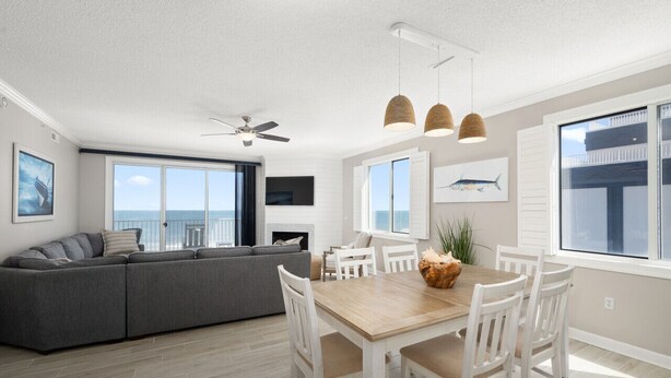A modern living room with a grey sectional sofa, a wooden dining table with white chairs, and a ceiling fan.