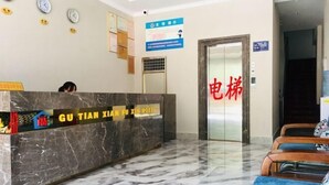 A hotel reception area with a marble reception desk, a sign for 'GU TIAN XIAN FU XIN HOYES', and a door labeled '电梯' (elevator). - Gutian Fuxin Hotel (Gutian)