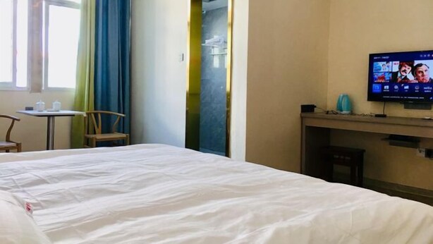 A hotel room with a bed, a desk, a chair, a TV, and a window with curtains. - Gutian Fuxin Hotel (Gutian)