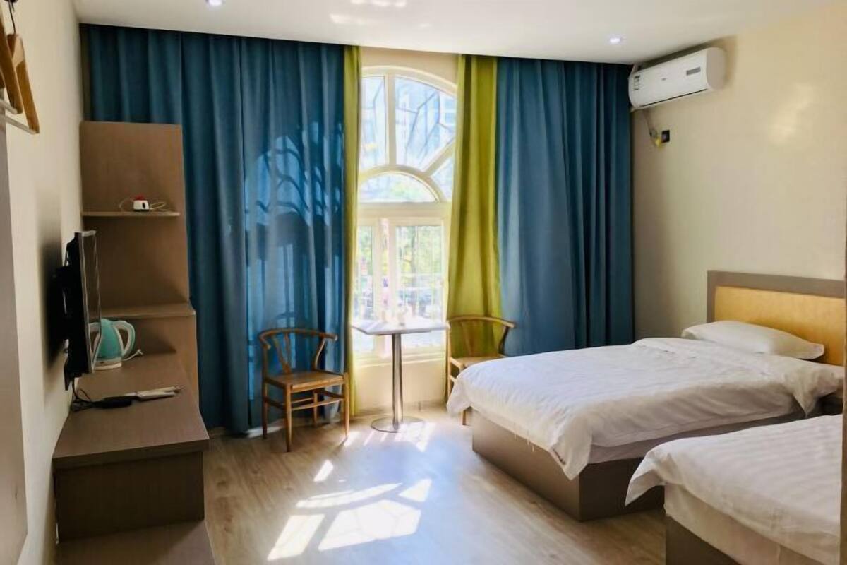 Una habitación de hotel con dos camas, un escritorio, una silla y un ventanal con cortinas.