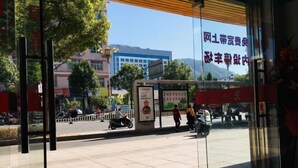A bus stop with a signboard, a red mat on the ground, and a view of a street with buildings and trees. - Gutian Fuxin Hotel (Gutian)