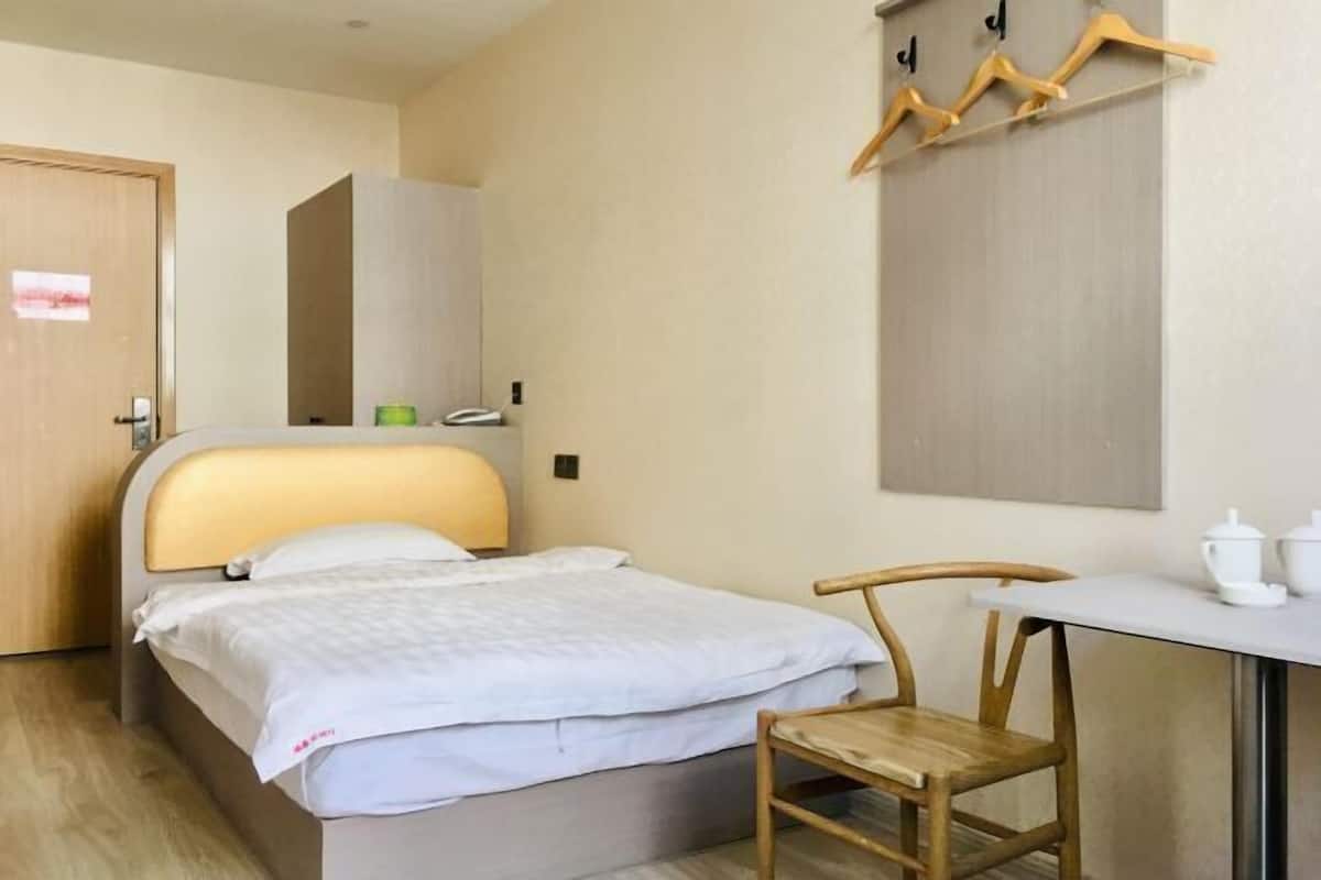 Una habitación de hotel con una cama, una silla de madera, una mesa con tetera y un perchero con ganchos.