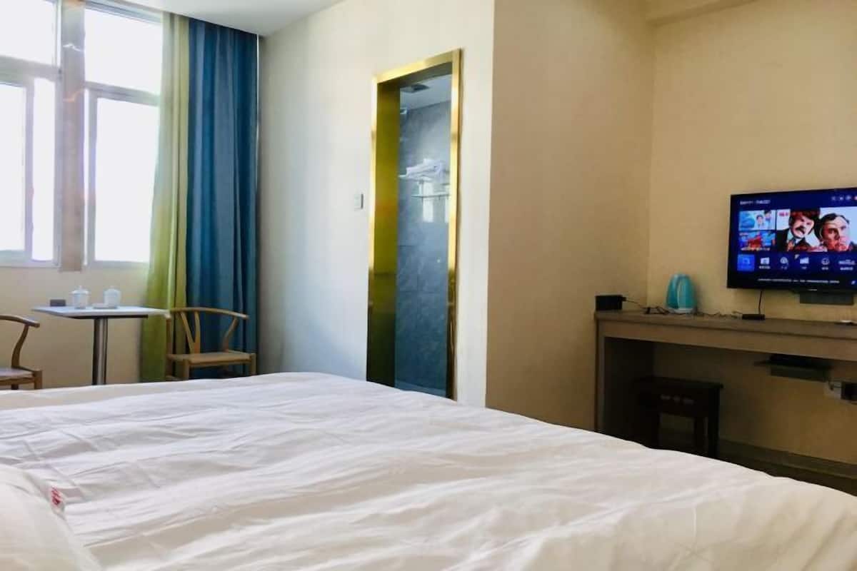 Una habitación de hotel con cama, escritorio, silla, televisión y ventana con cortinas.