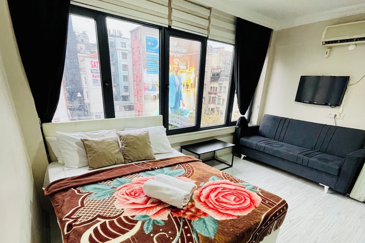 Ein Hotelzimmer mit einem Bett, einer Couch, einem Fernseher und einem Fenster mit Blick auf die Stadt.