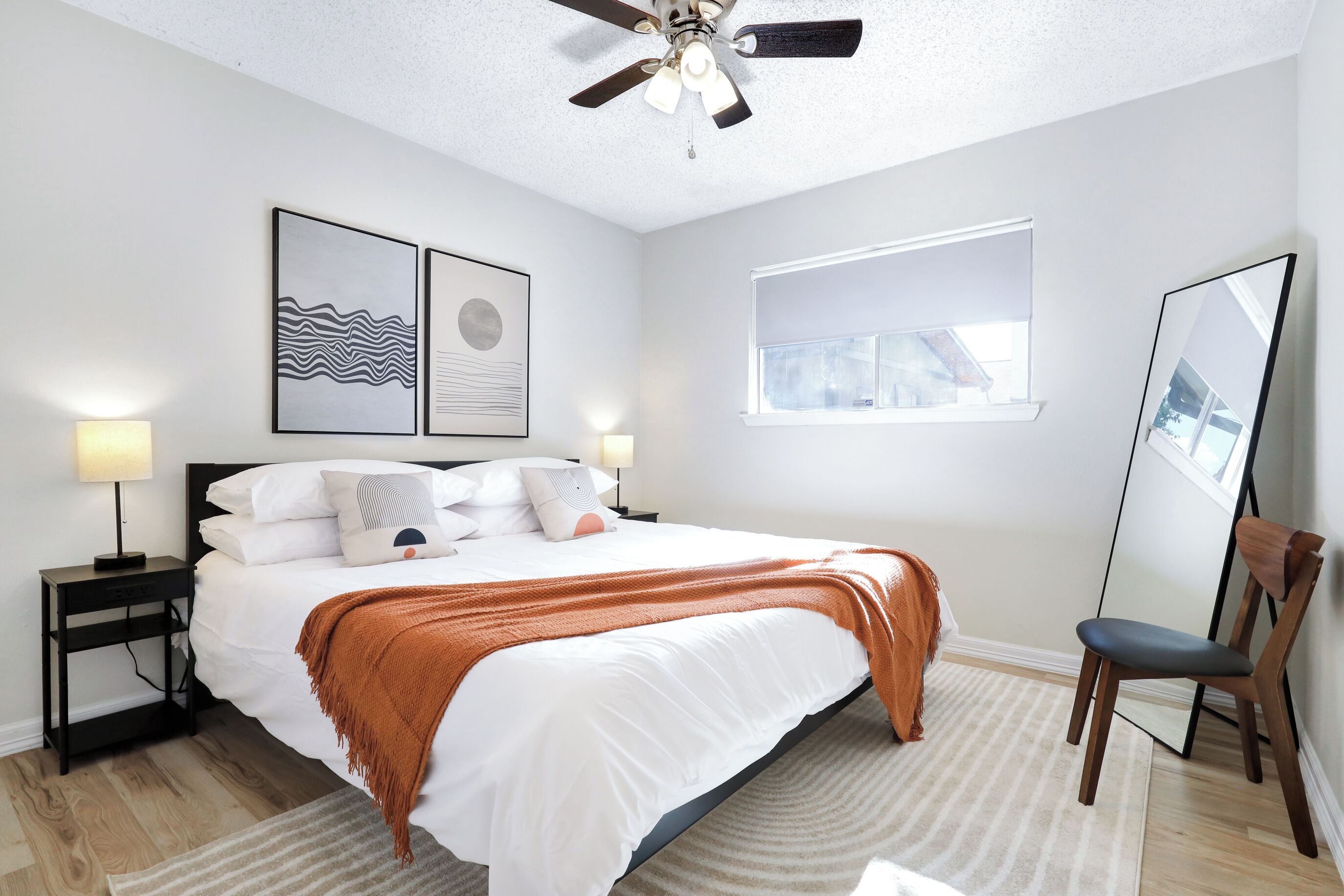 A bedroom with a bed, nightstands, a ceiling fan, a window, and artwork on the wall.