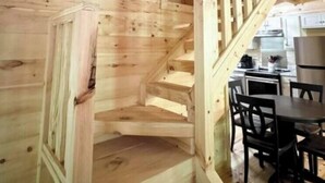 A wooden staircase with a railing leading to an upper level. Below, there is a dining area with a table and chairs. - Robin's Nest Sleeps 6 (Mentone)