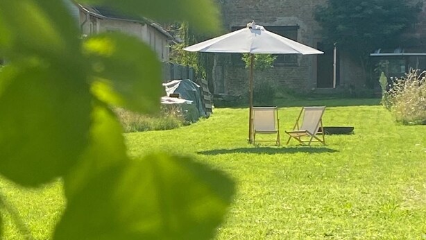 En trädgård med en gräsmatta, ett utemöblemang med ett bord och två stolar samt ett parasoll.