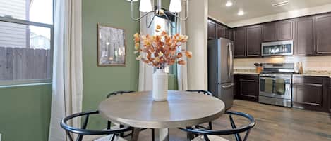A modern kitchen with dark cabinets, stainless steel appliances, and a round dining table with chairs.