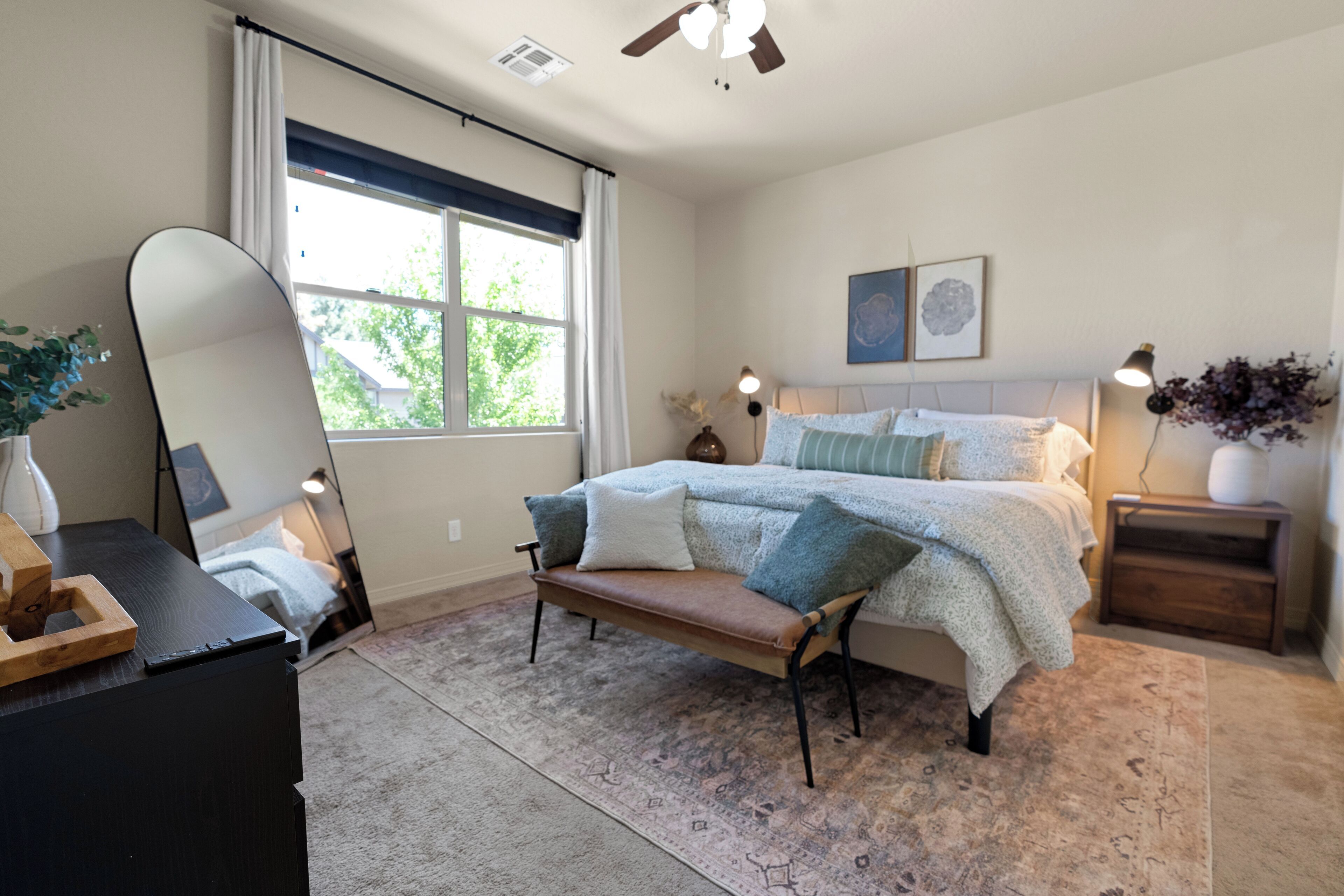 Une chambre à coucher avec un lit, des tables de chevet, un miroir, une fenêtre avec des rideaux et un tapis.