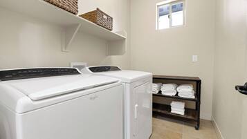 Uma área de lavanderia com duas máquinas de lavar Whirlpool brancas, uma prateleira com cestos e outra prateleira com toalhas dobradas.