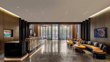 A modern lobby with a reception desk, seating area, and large windows.