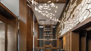 A modern interior with a reception desk, wooden paneling, and a unique ceiling light fixture. - Fengdu Hotel (Harbin) (Harbin)