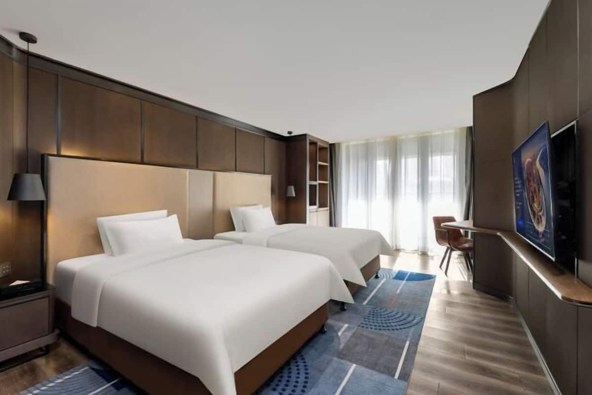A hotel room with two beds, a TV, a desk, and a chair.