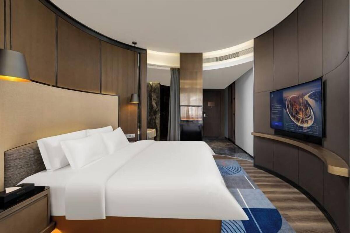 A hotel room with a bed, a nightstand, a TV, and a curved wall design.