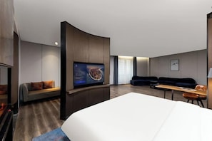 A modern hotel room with a large bed, a flat-screen TV mounted on a wall, a sofa, a small table, and a seating area with a couch and chairs. - Fengdu Hotel (Harbin) (Harbin)