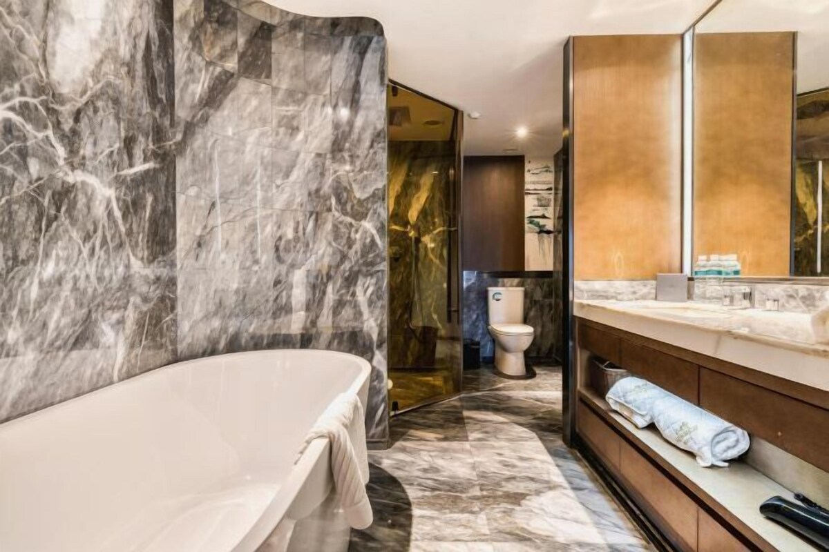 A modern bathroom with a marble wall, a freestanding bathtub, a vanity with a mirror, and a toilet.