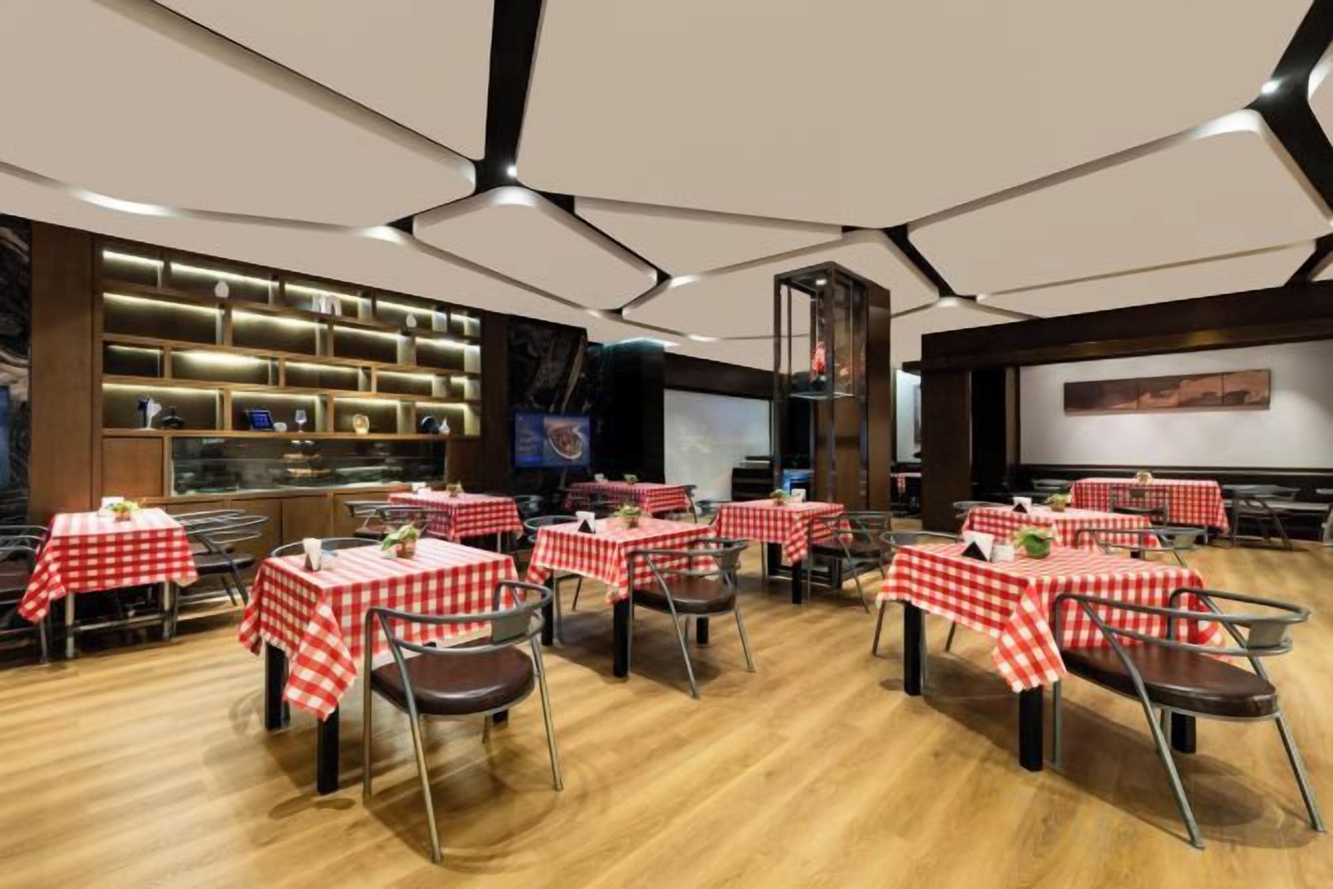 A restaurant with multiple tables covered in red and white checkered tablecloths, wooden flooring, and a modern ceiling design.