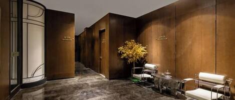 A hotel lobby with a marble floor, wooden paneling, a reception desk, and a seating area.