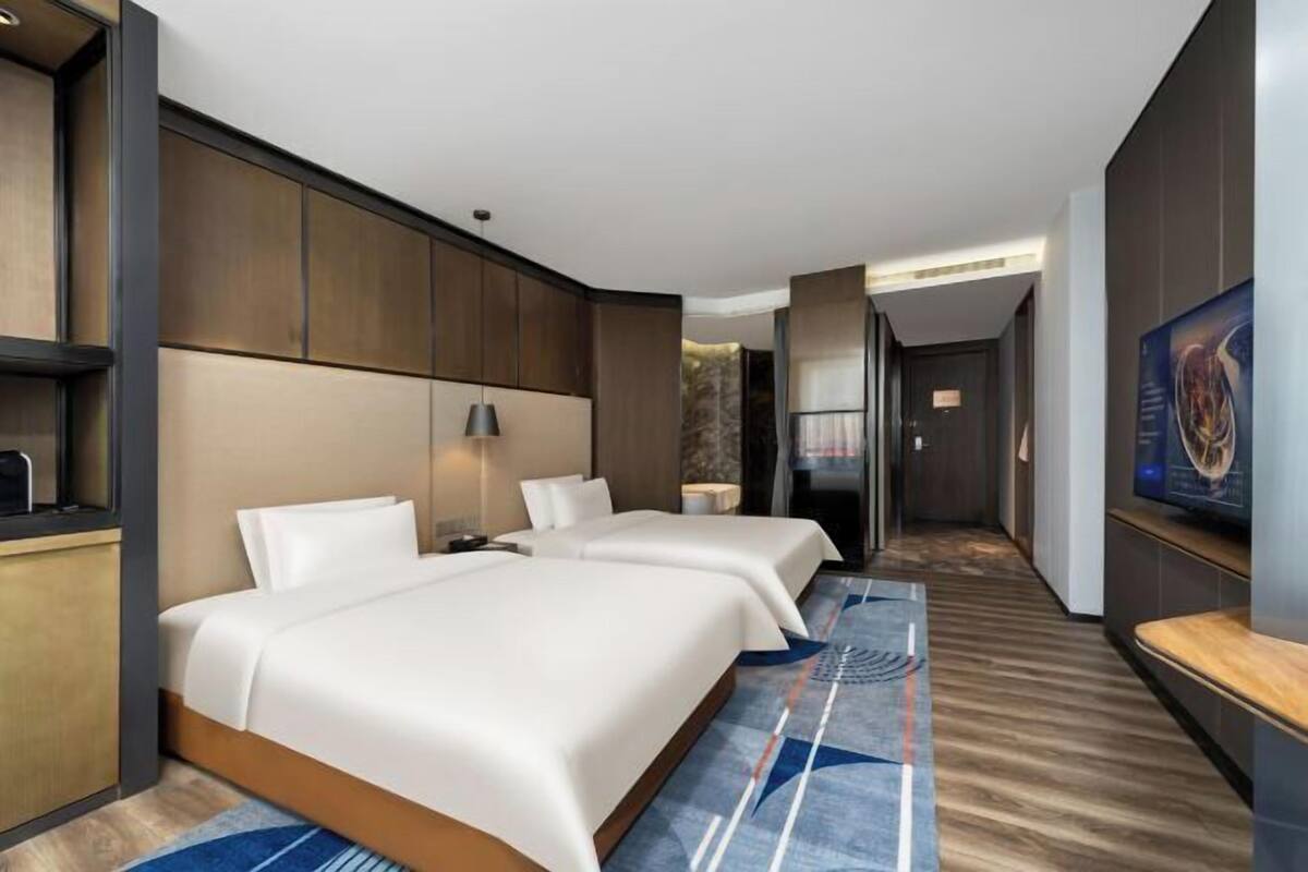 A hotel room with two beds, a desk, a TV, and a large painting on the wall.