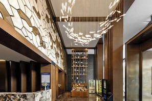 Um hall moderno com uma recepção de mármore, uma parede decorativa, uma estante central e um elevador de vidro.