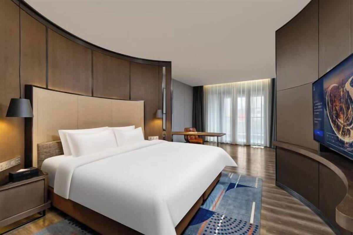 A modern hotel room with a large bed, a desk, and a television.