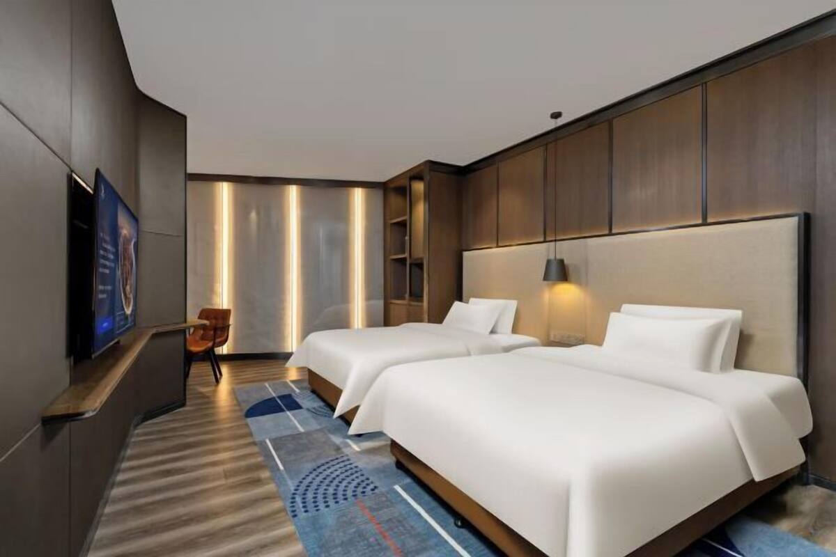 A hotel room with two beds, a TV, a desk, and a chair.