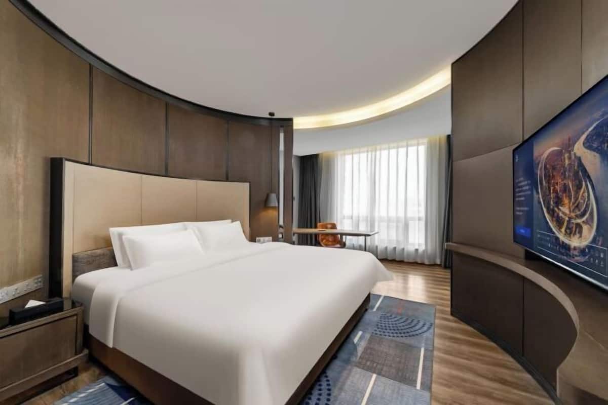 A modern hotel room with a large bed, a flat-screen TV, and a curved wall design.